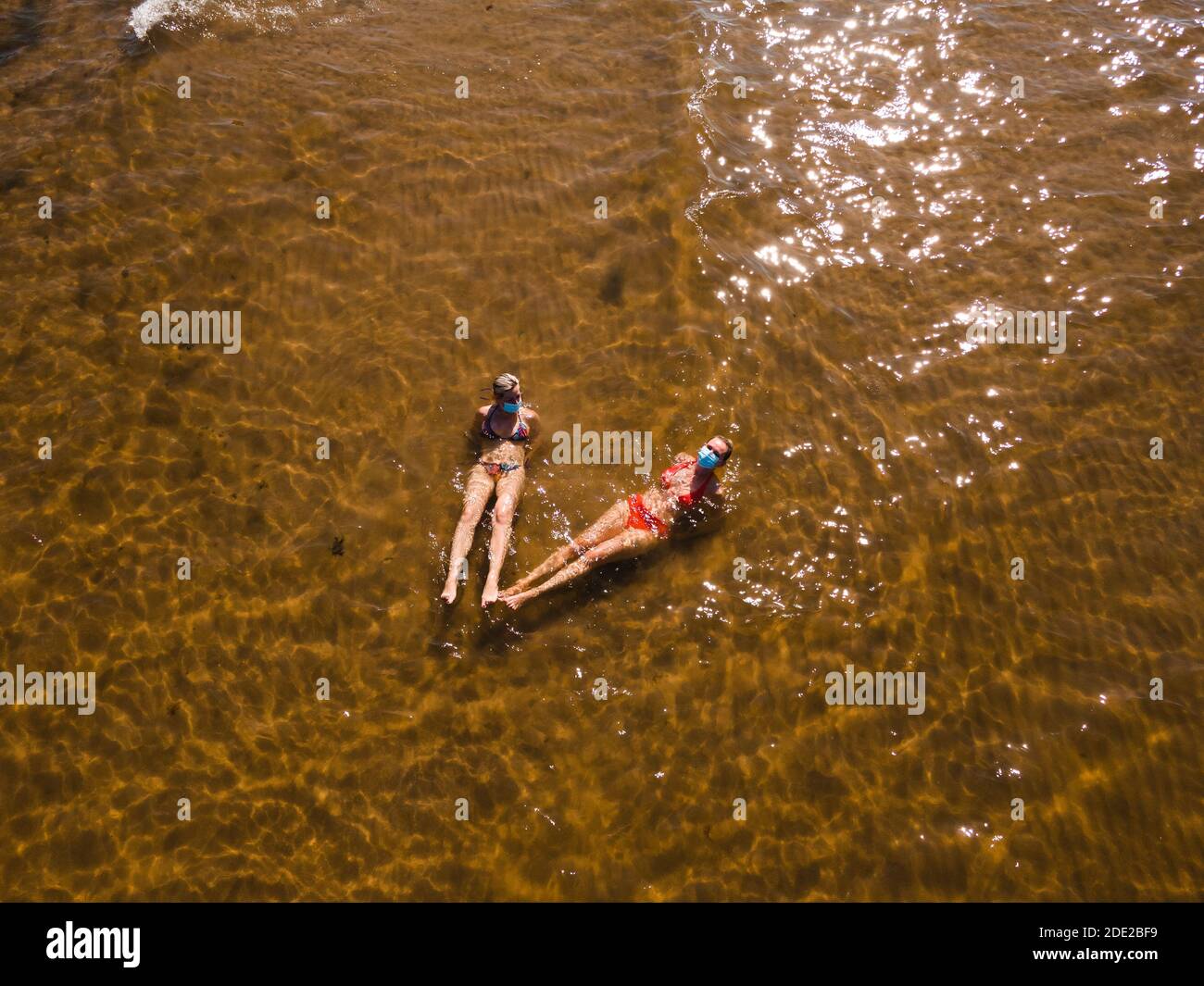 Vue aérienne: Deux femmes s'amusant en mer portant des masques médicaux Banque D'Images