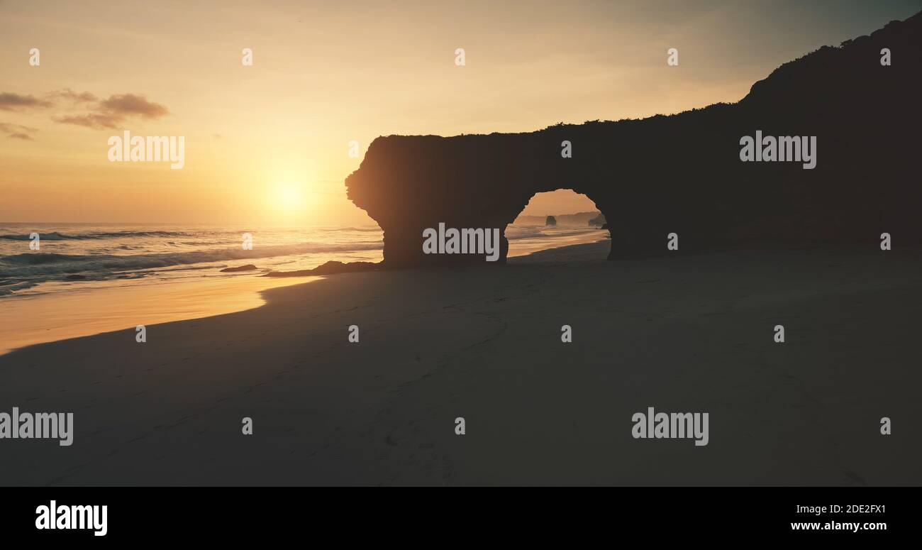 Silhouette de soleil de mur de roche avec trou géant sur plage de sable vue aérienne. Côte sablonneuse de l'océan, falaise unique à l'île de Sumba, Indonésie, Asie. Personne la nature à la lumière du soleil. Coucher de soleil d'été cinématographique Banque D'Images