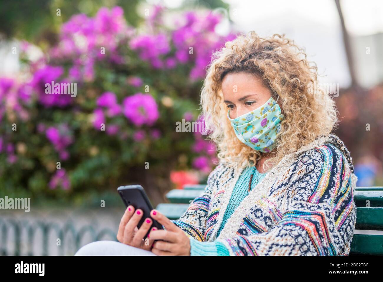 Adultes avec masque médical facial pour l'urgence du coronavirus covid-19 protection extérieure - une femme regarde le téléphone pendant une urgence covid-19 Banque D'Images