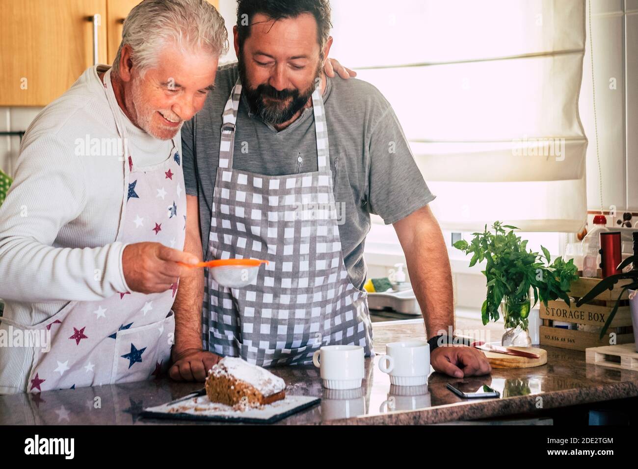 Couple d'adultes et d'hommes âgés père et fils ou les amis cuisent ensemble à la maison dans la cuisine en s'amusant - activité de boulangerie à la maison avec différents âges Banque D'Images