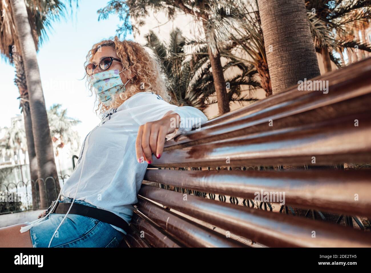 Une femme s'assoit sur un banc portant un masque médical pour les épidémies de protection du coronavirus covid-19 - concept de restrictions extérieures pour lutter contre la pandémie Banque D'Images