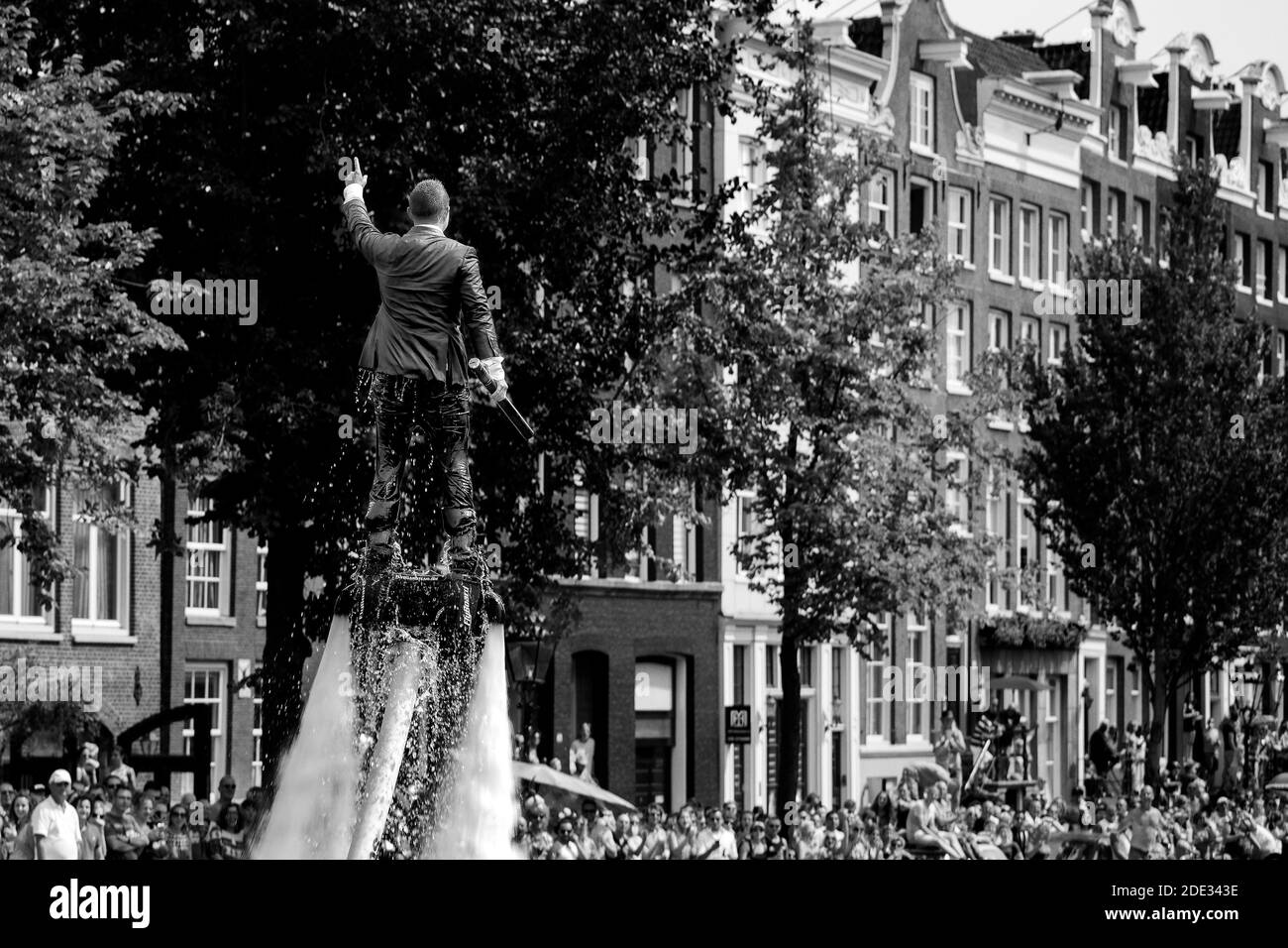 L'homme en flyboard en costume mouillé s'élève bien au-dessus de la foule pendant la fierté gay dans les canaux d'Amsterdam. Photographie en noir et blanc. Banque D'Images