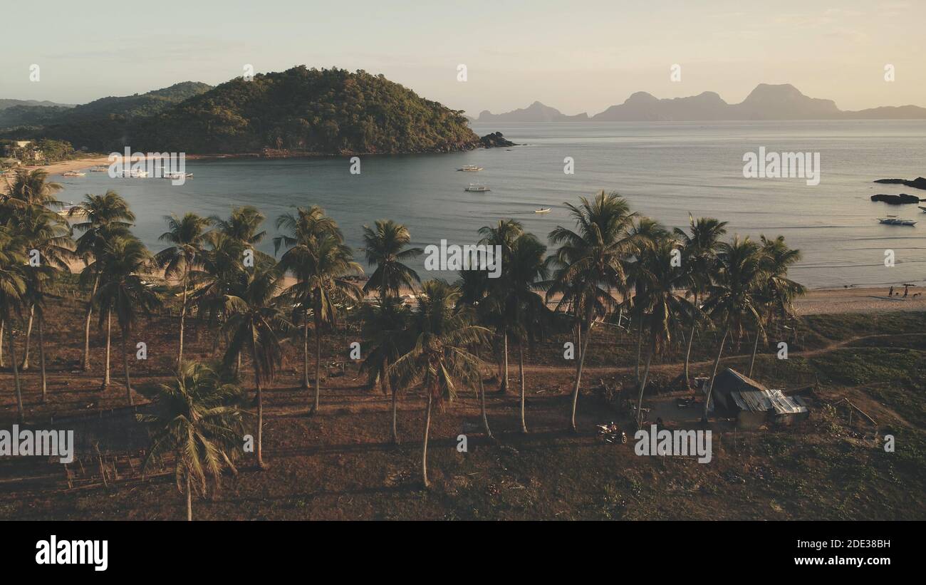 Bateau traditionnel à l'antenne verte de la côte. Les touristes se reposent sous les palmiers. Plage de sable à la baie océanique avec des navires et des navires. Les gens marchent sur la côte de sable. Croisière d'été aux Philippines Banque D'Images