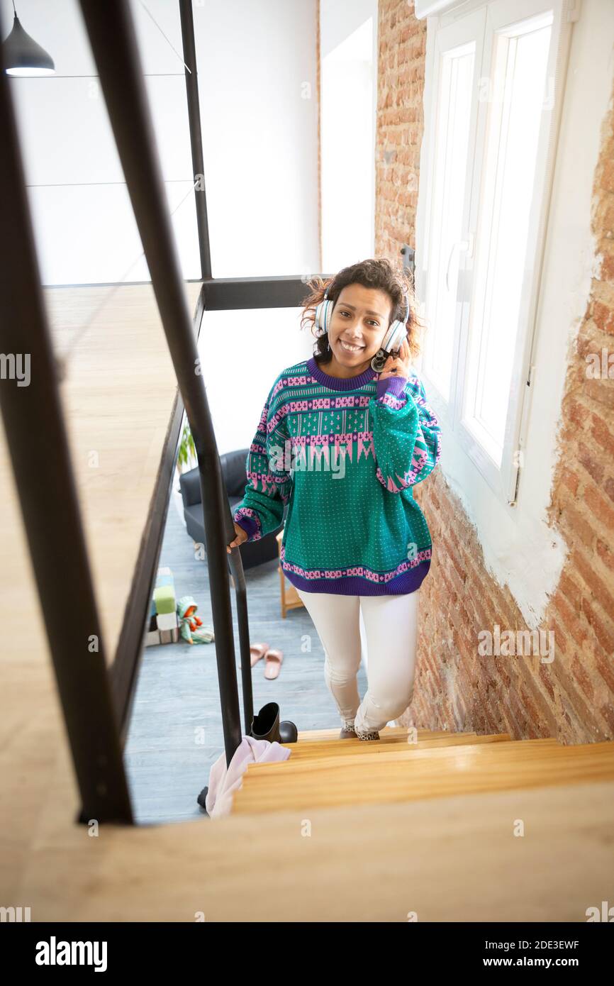 Jeune fille souriante marchant dans les escaliers à l'intérieur de sa maison. Elle porte un casque. Espace pour le texte. Banque D'Images