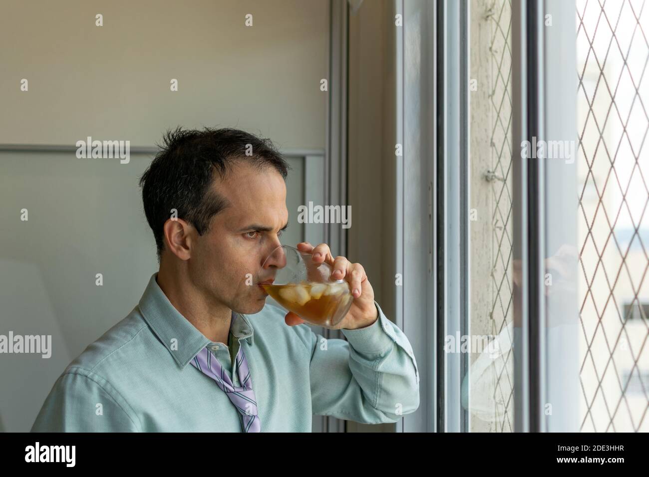 Homme mature (44 ans) regardant la fenêtre et buvant du whisky. Banque D'Images