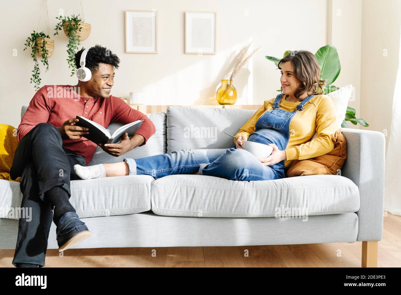 Femme enceinte mangeant sur le canapé avec son mari qui écoute de la  musique et lit un livre. Concept de couple interracial Photo Stock - Alamy