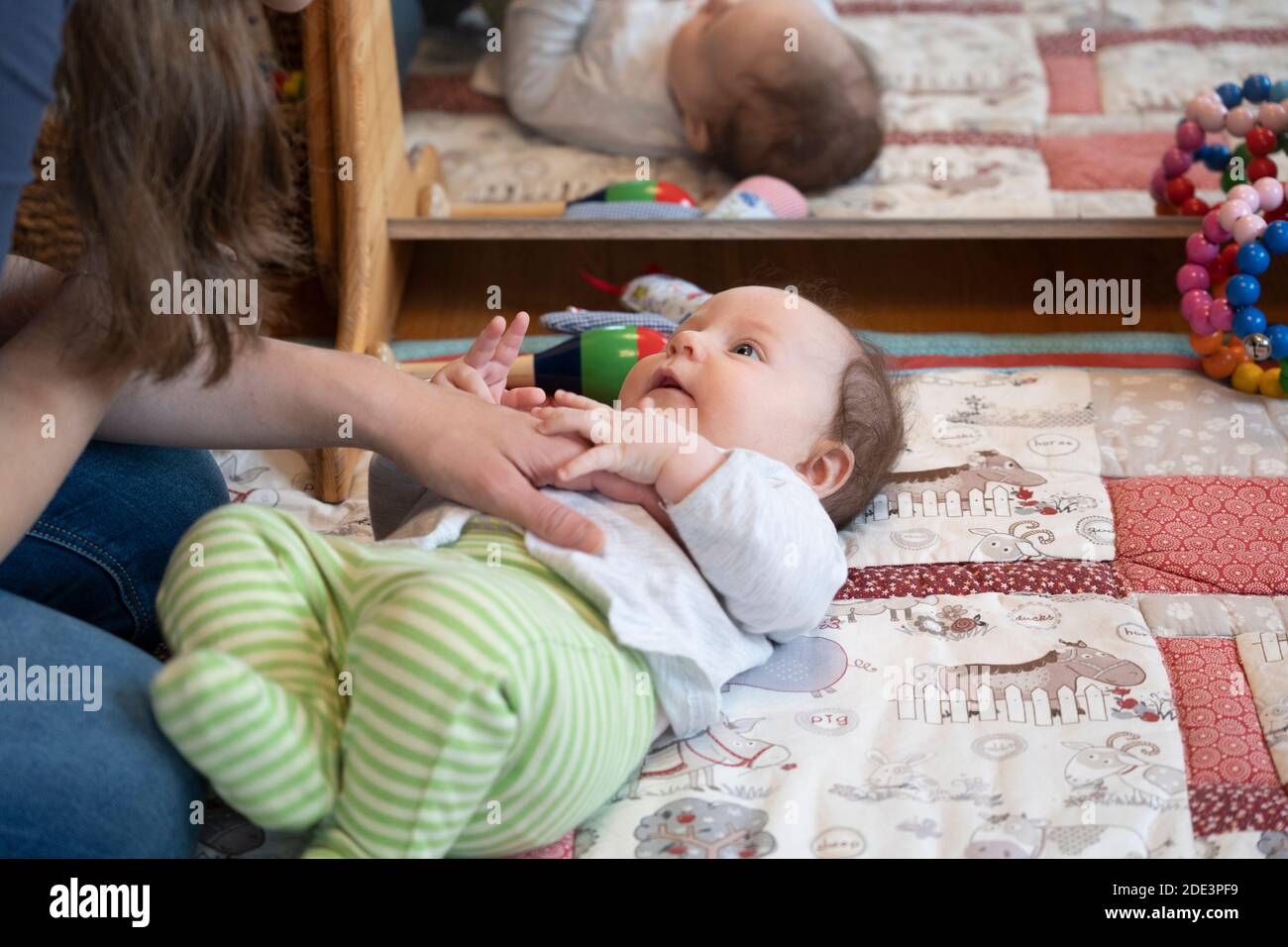 Une mère interagissant et jouant avec sa fille de 4 mois, les deux allongé sur un tapis de jeu avec un miroir derrière, Royaume-Uni Banque D'Images