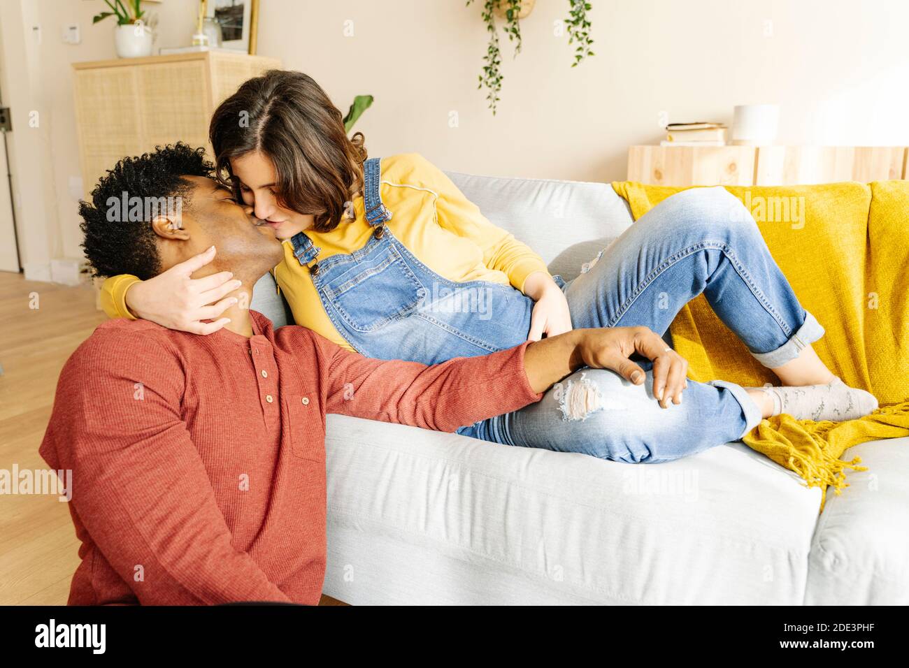 Mari embrassant sa femme enceinte sur un canapé. Concept de couple interracial Banque D'Images