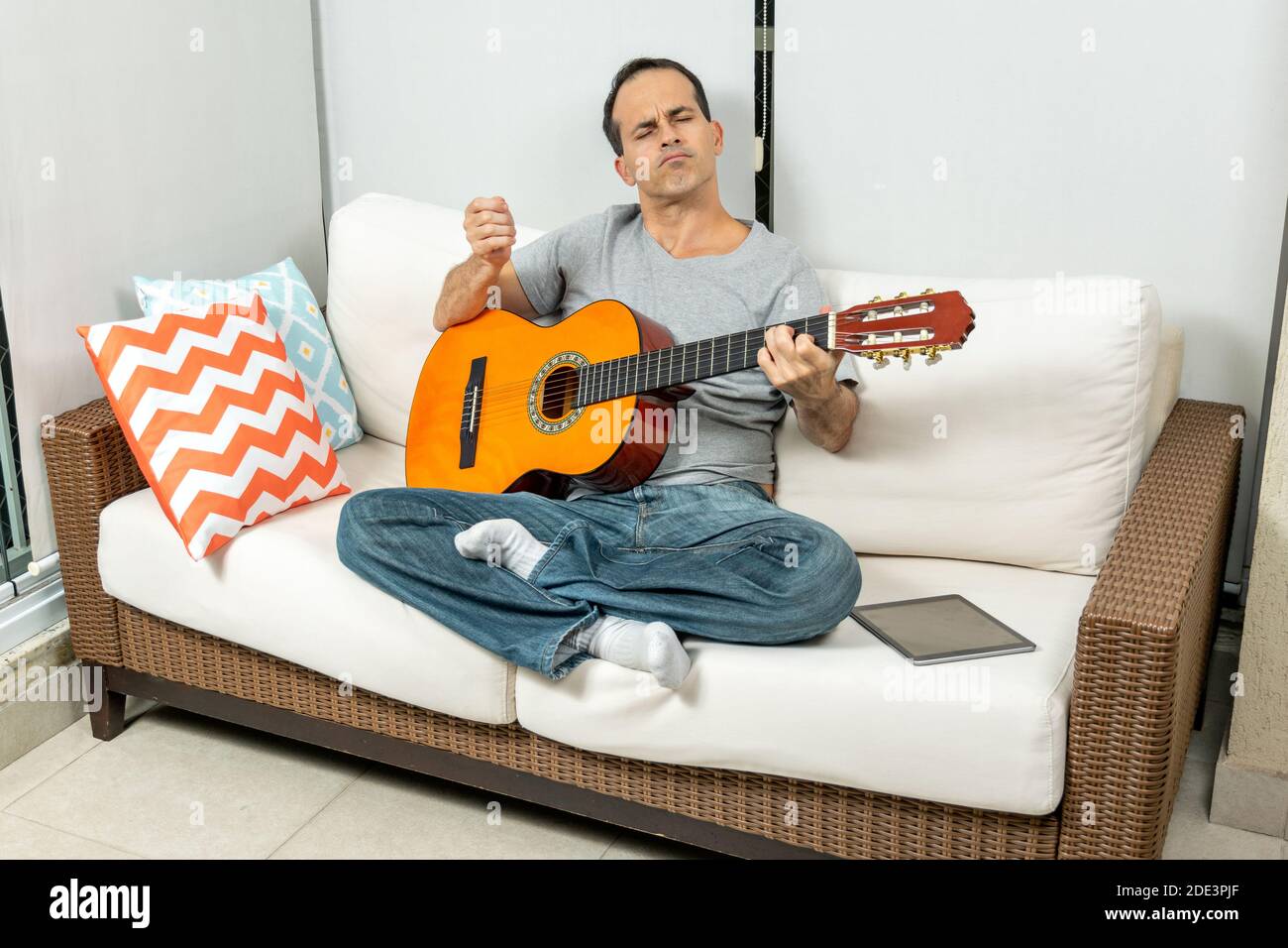 Homme mature assis sur le canapé et jouant de la guitare avec sensation. Banque D'Images