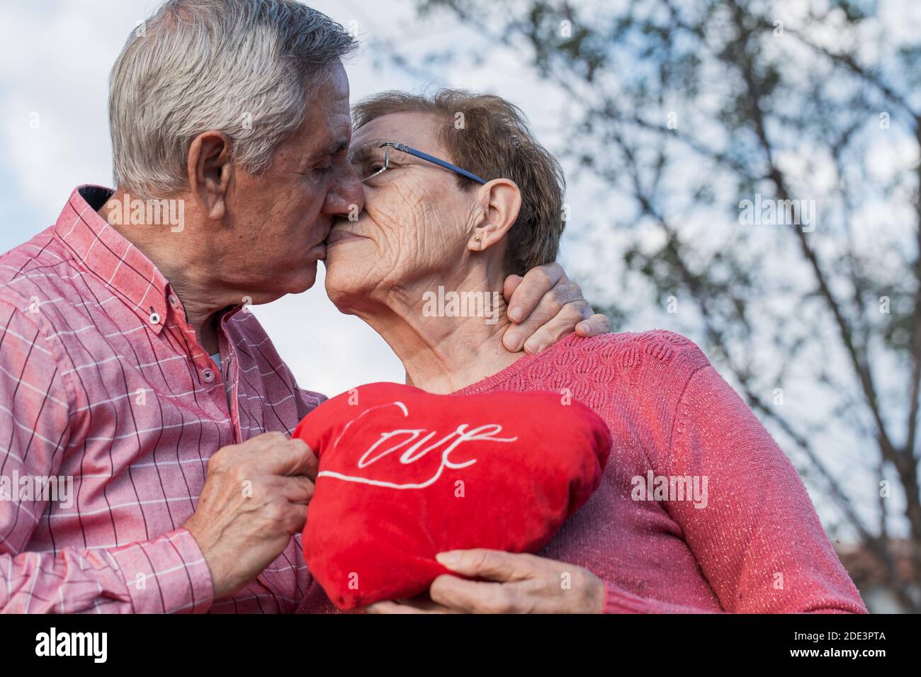 Vue latérale à angle bas d'un couple senior charmant et romantique avec Cœur rouge embrassant et embrassant doucement tout en célébrant l'anniversaire de mariage R Banque D'Images