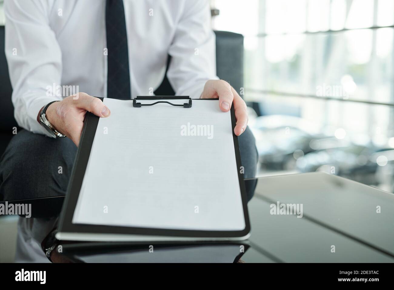 Mains du jeune Manager du centre de voiture tenant le presse-papiers avec document de vente d'une des automobiles et de la montrer à client avant la signature Banque D'Images