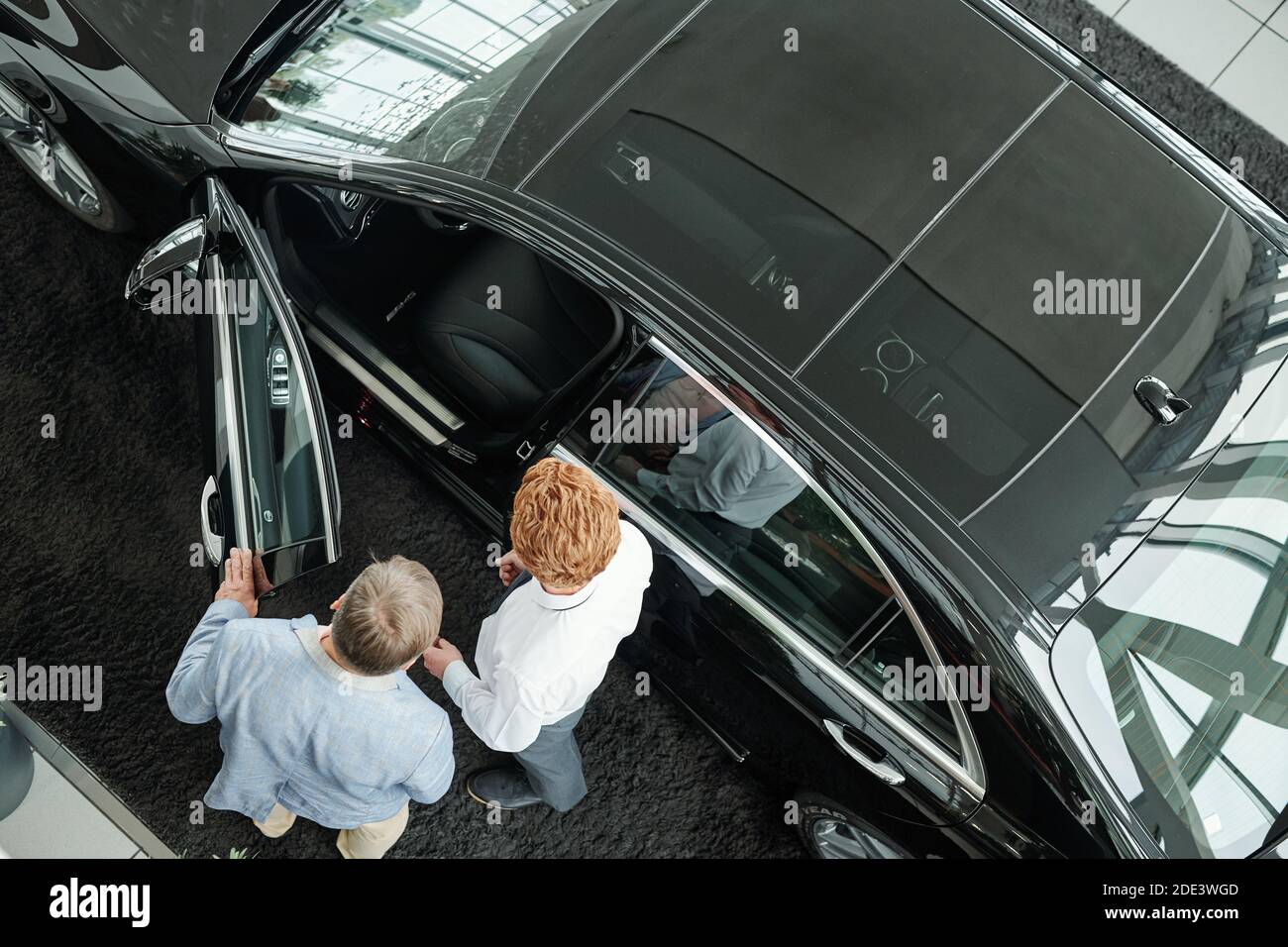 Vue du jeune vendeur de l'auto centre ouvrant la porte de véhicule noir  tout en montrant et en décrivant les caractéristiques de la voiture  intérieur pour client masculin Photo Stock - Alamy