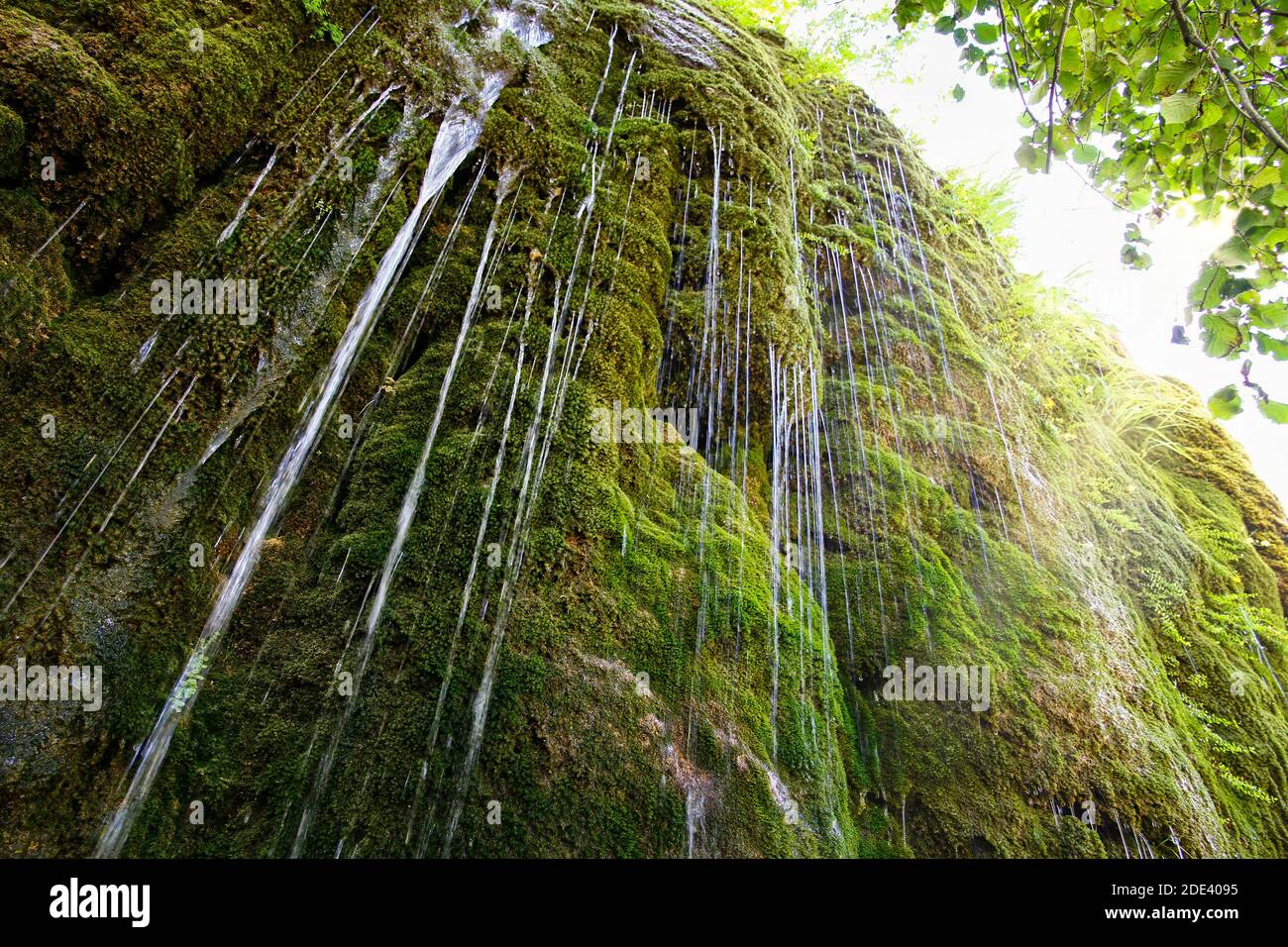 L'eau s'écoulant d'une roche recouverte de mousse vue d'en dessous avec un ciel ensoleillé en arrière-plan, source d'eau naturelle pure dans les Pyrénées Banque D'Images