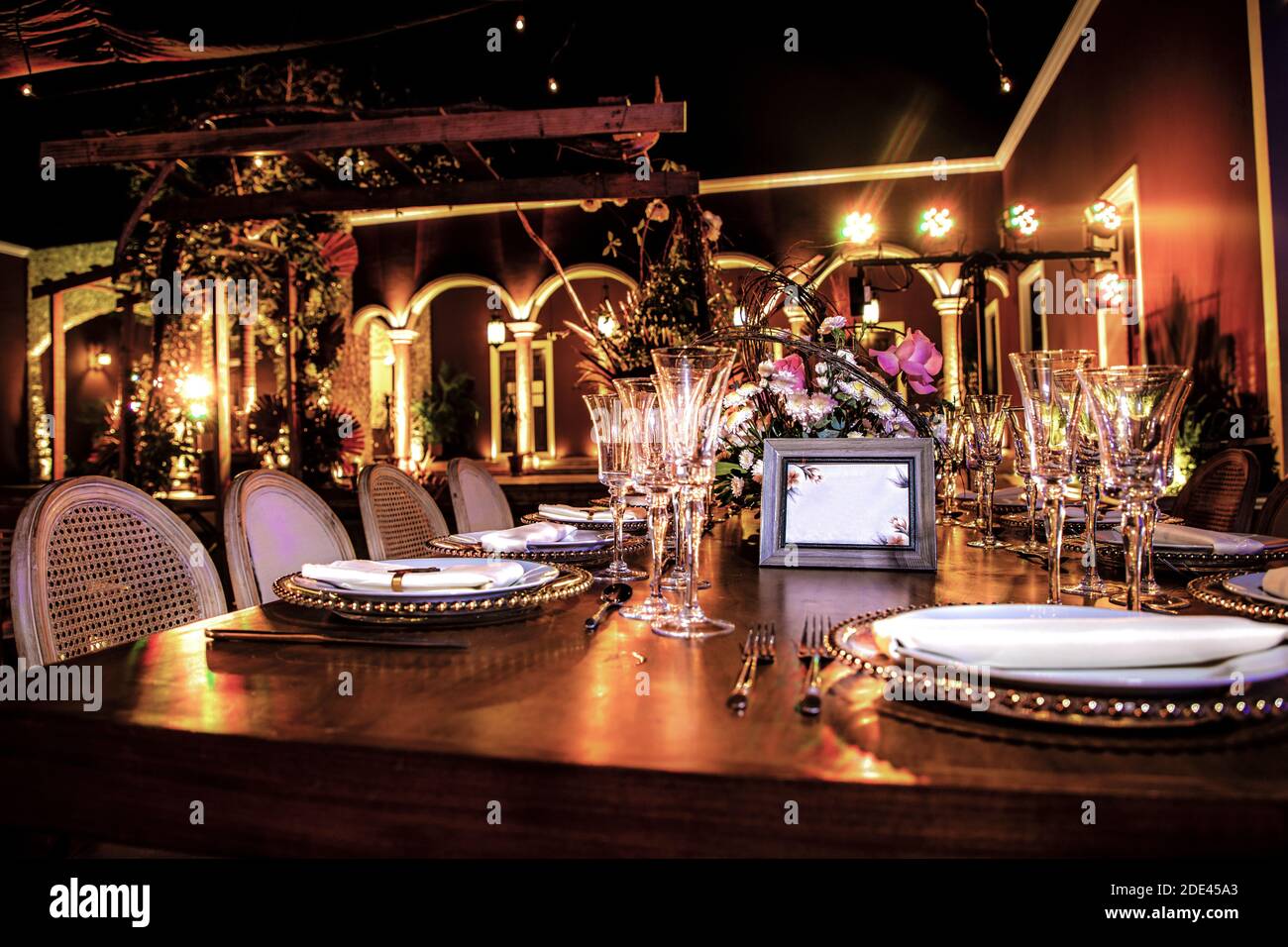 Table en bois montée avec des plaques et de belles lunettes pour une illusion, ornée de fleurs et de lumières dans une Hacienda la nuit Banque D'Images