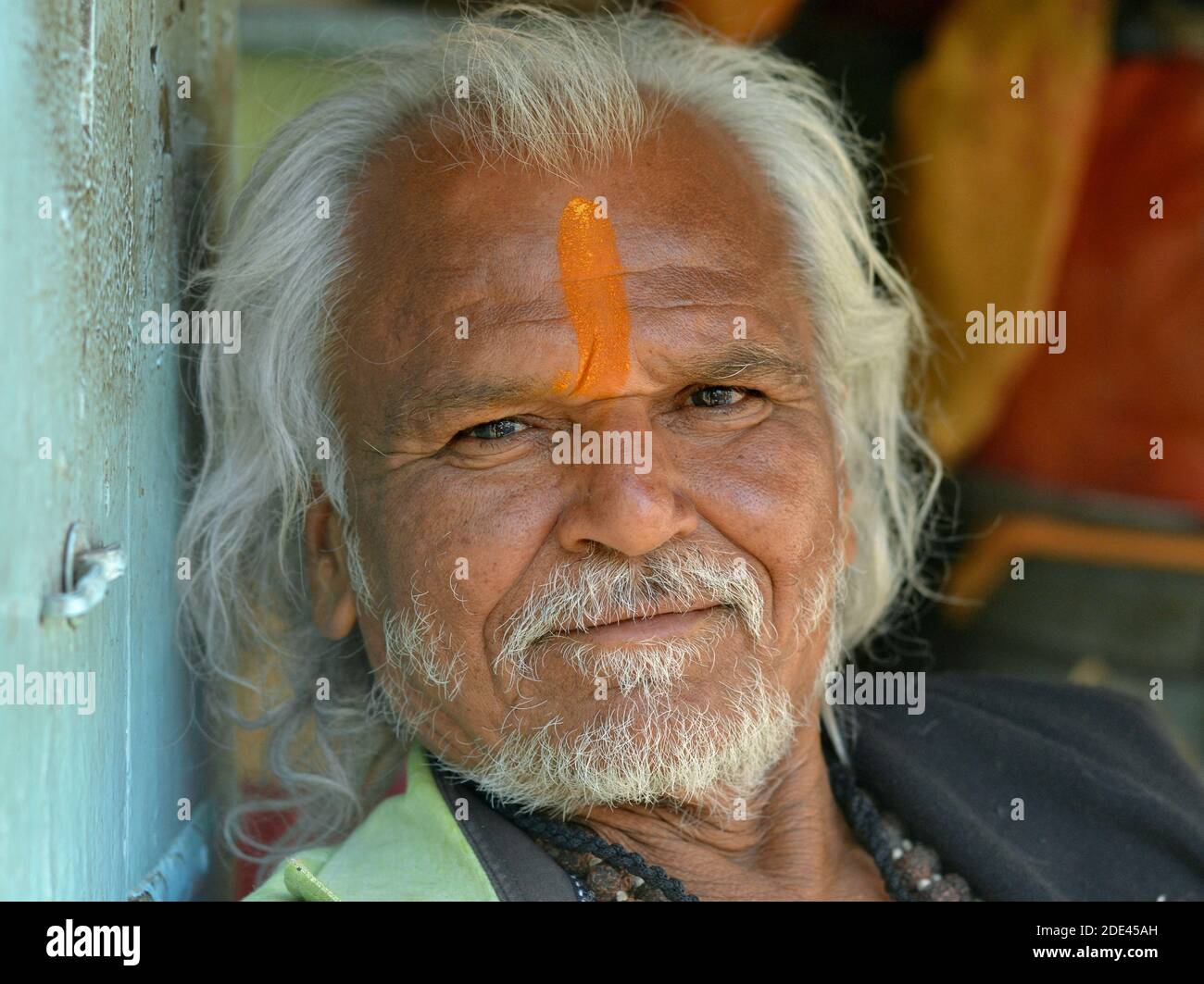 Dévot hindoue indienne âgée avec une marque verticale orange tilak sur son front et de longs cheveux blancs poses pour la caméra. Banque D'Images