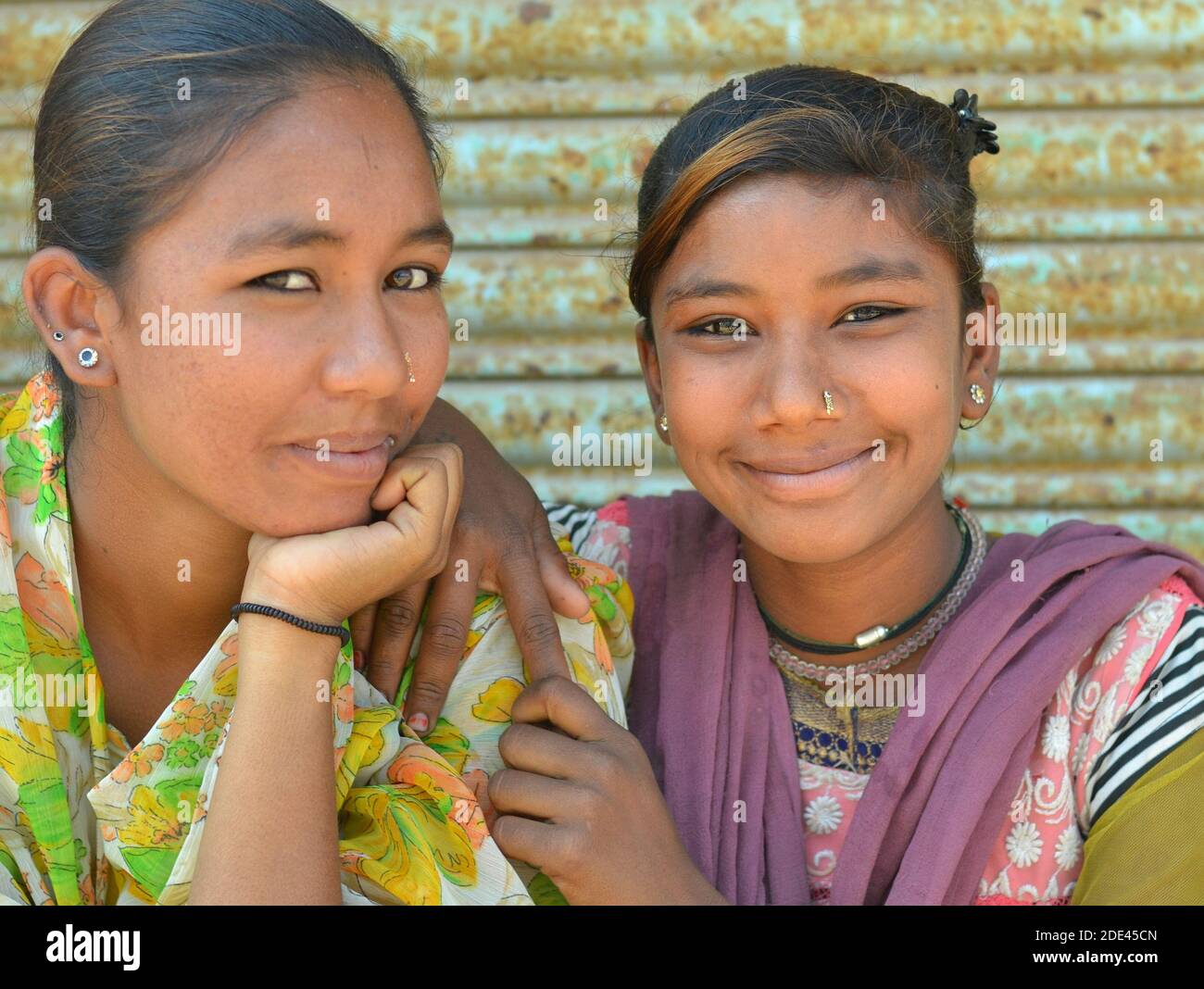Deux filles gujarati indiennes et sympathiques de Kutch se posent ensemble pour l'appareil photo devant un arrière-plan de volet en acier rouillé. Banque D'Images