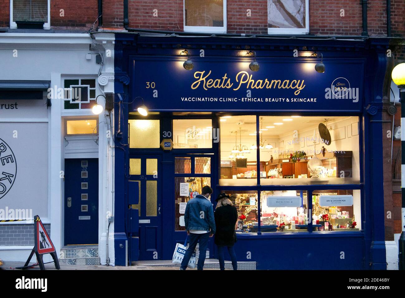 Couple regardant la fenêtre du magasin de la pharmacie affichant un panneau sur la grippe et le vaccin contre le covid19. Keats Pharmacy, Hampstead, Londres. Banque D'Images