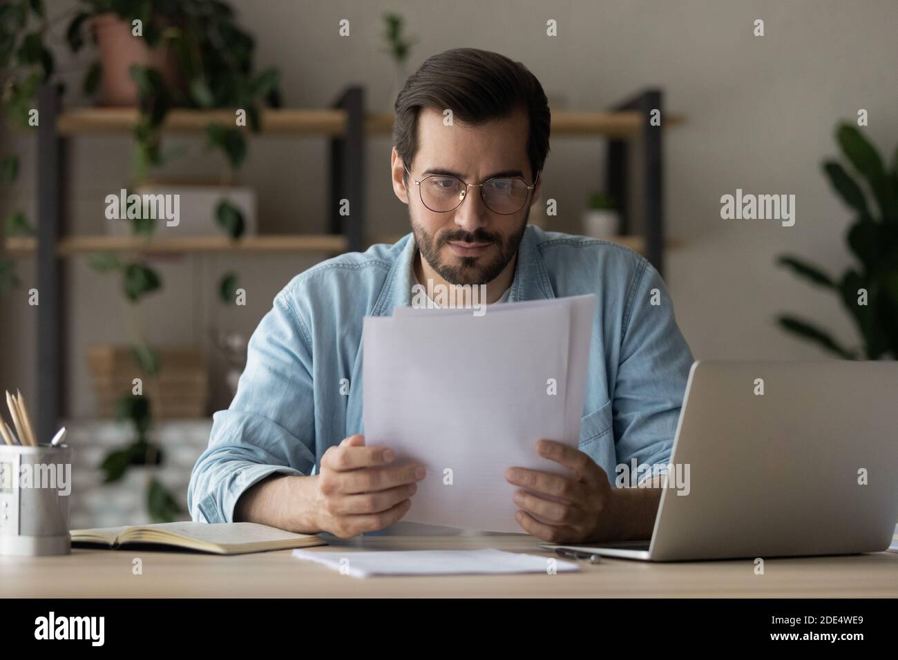 Un homme pensif s'assoit au bureau pour lire un document papier Banque D'Images