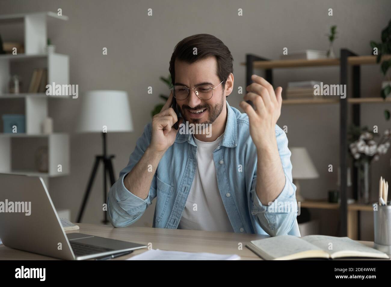 Un homme heureux s'assoit au bureau et parle sur un smartphone Banque D'Images