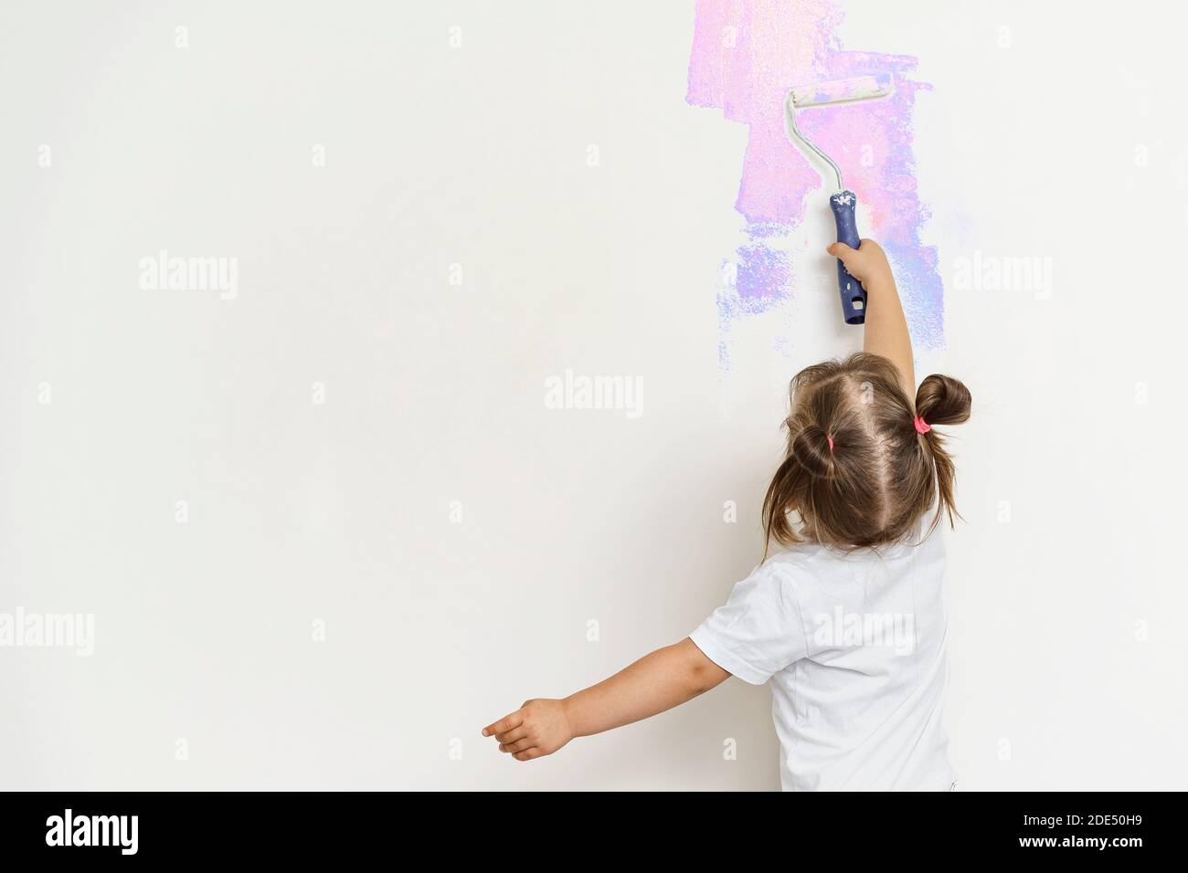 jolie petite fille peint le mur gris avec une construction rouleau aux couleurs vives Banque D'Images