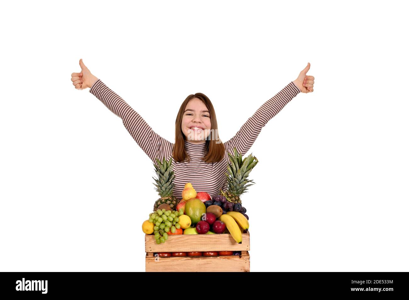 bonne fille avec des fruits dans une caisse en bois et pouces vers le haut Banque D'Images