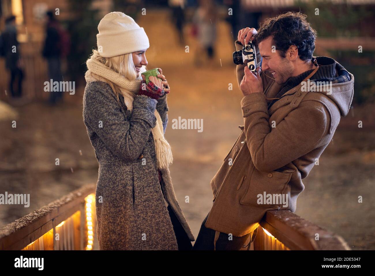 jeune homme caucasien prenant une photo de sa petite amie tenant une tasse de thé à l'extérieur avec l'ancien appareil photo. concept de christmastime Banque D'Images