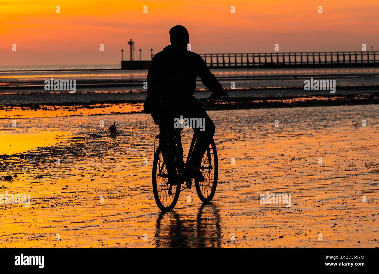 Un cycliste prend un vélo sur la plage pendant une soirée d'hiver tandis que le soleil se couche à marée basse à Littlehampton, West Sussex, Angleterre, Royaume-Uni. Banque D'Images