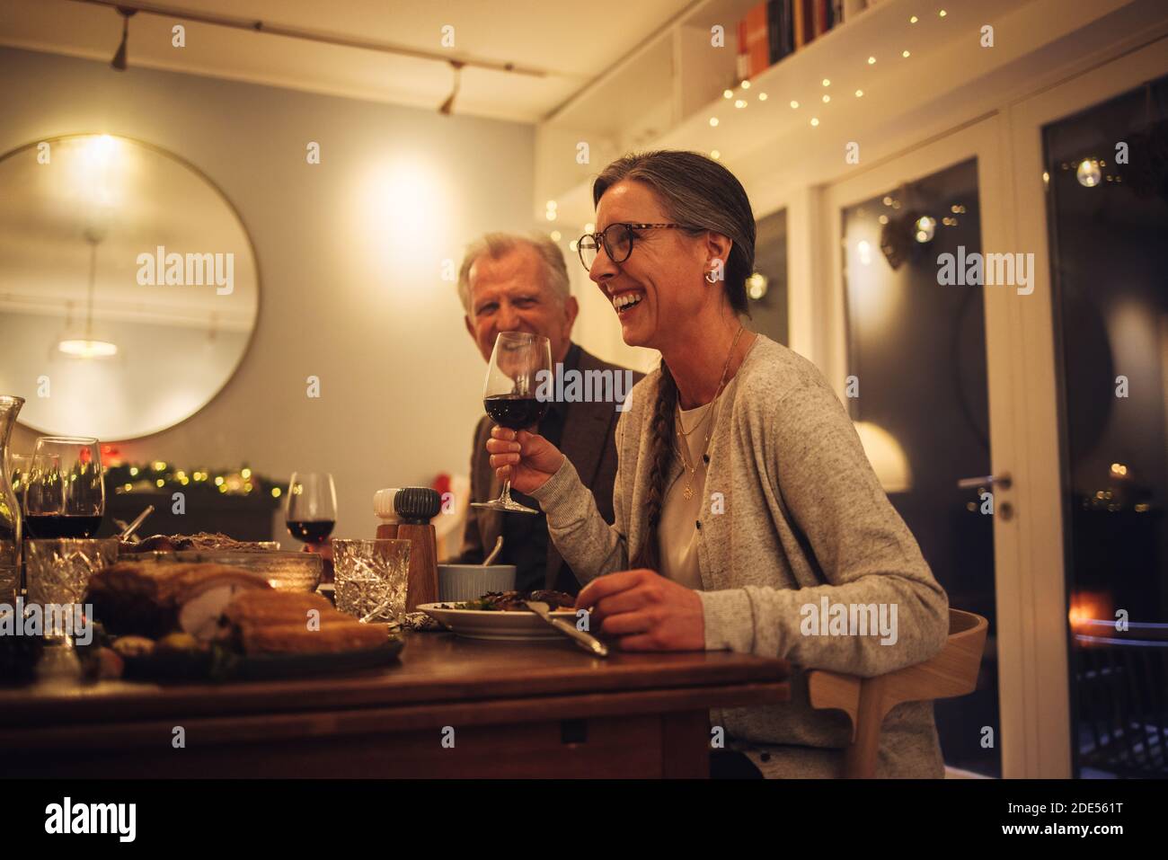 Couple senior appréciant un dîner de noël en famille. Femme mature tenant un verre de vin parlant et souriant à la table du dîner. Banque D'Images