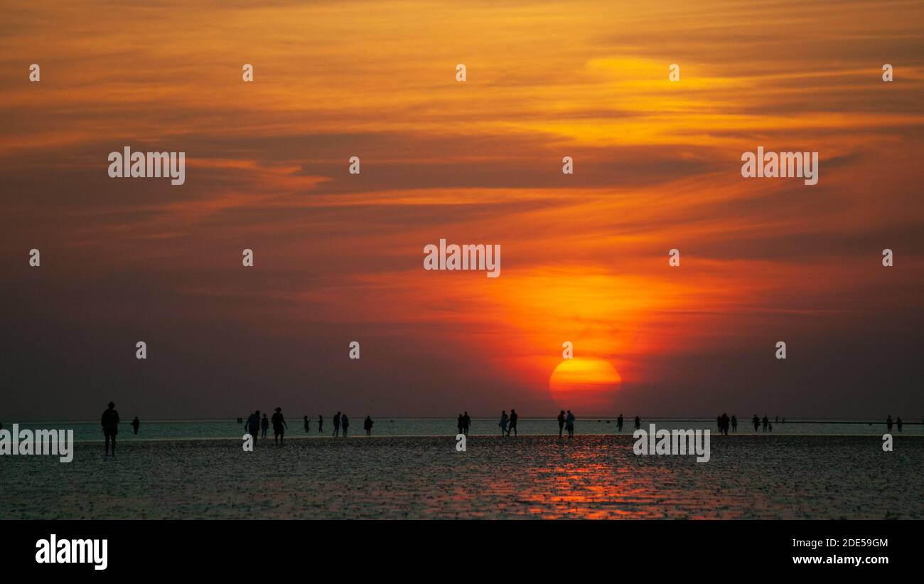 Panorama avec silhouettes de personnes à la plage et watt devant le soleil couchant. Une scène d'été. Banque D'Images