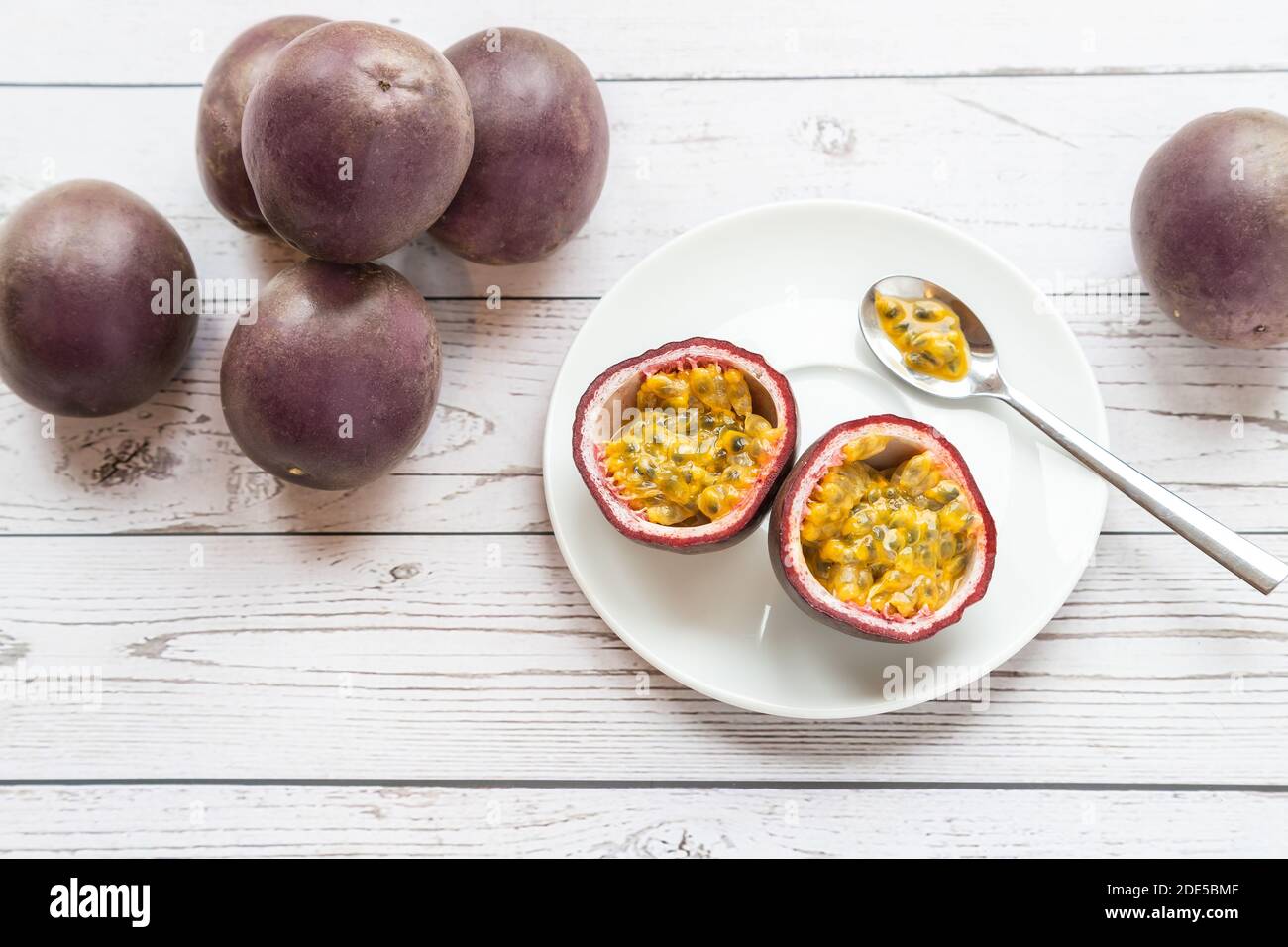 fruit de la passion mûr dans une assiette sur une table en bois blanc, on est coupé et prêt-à-manger avec une cuillère Banque D'Images