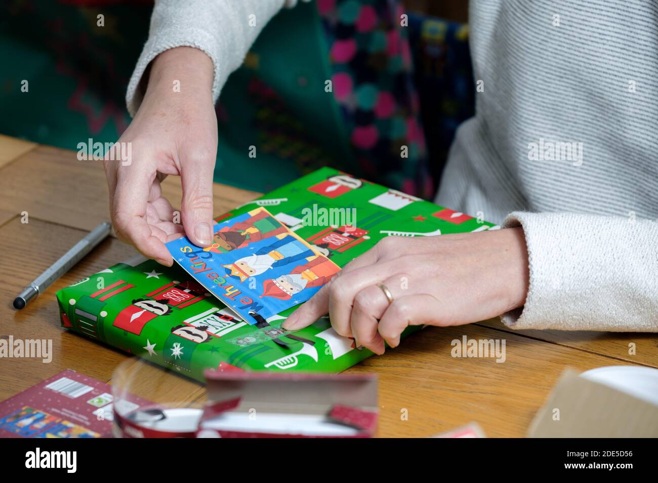 Une femme ajoute une étiquette cadeau à un cadeau de Noël elle vient de s'emballer dans du papier d'emballage de couleurs vives Banque D'Images