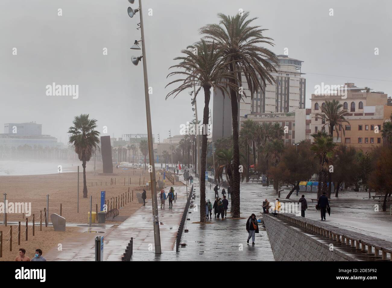 Les gens qui marchent le long de la plage par une journée froide, humide, terne, Barcelone, Espagne. Banque D'Images