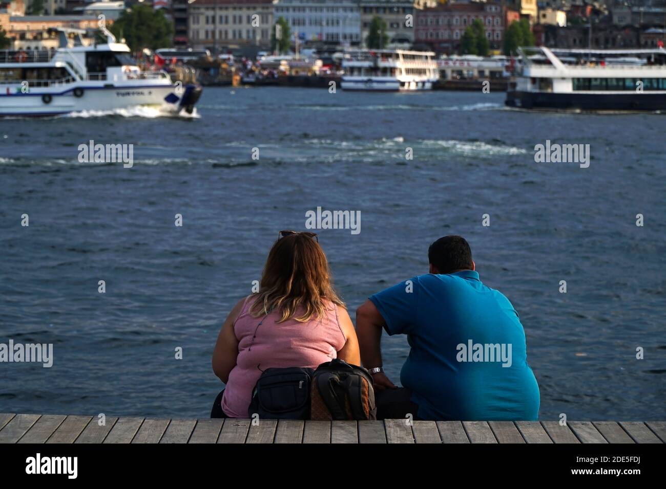 Istanbul, Turquie - 13 juillet 2019 : un jeune couple obèse est assis et regarde le paysage à la Corne d'Or, Istanbul. Il y a aussi des bateaux de visite. Banque D'Images