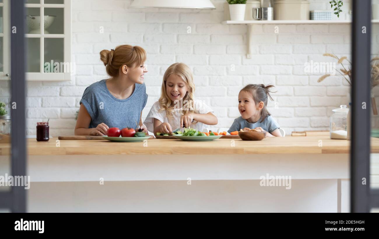 Une mère souriante et deux petites filles cuisent une salade ensemble Banque D'Images