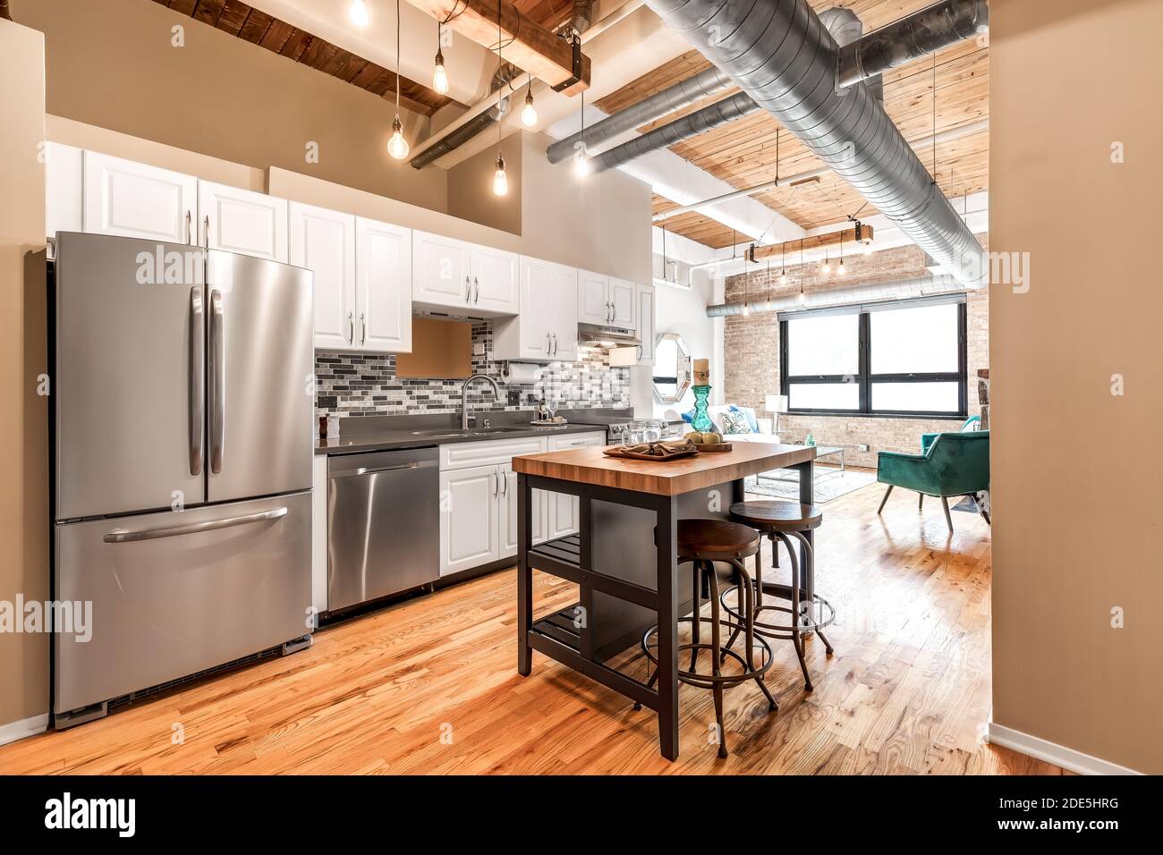Un appartement moderne avec un plafond exposé, des armoires blanches, et une vue sur un salon avec de grandes fenêtres lumineuses. Banque D'Images
