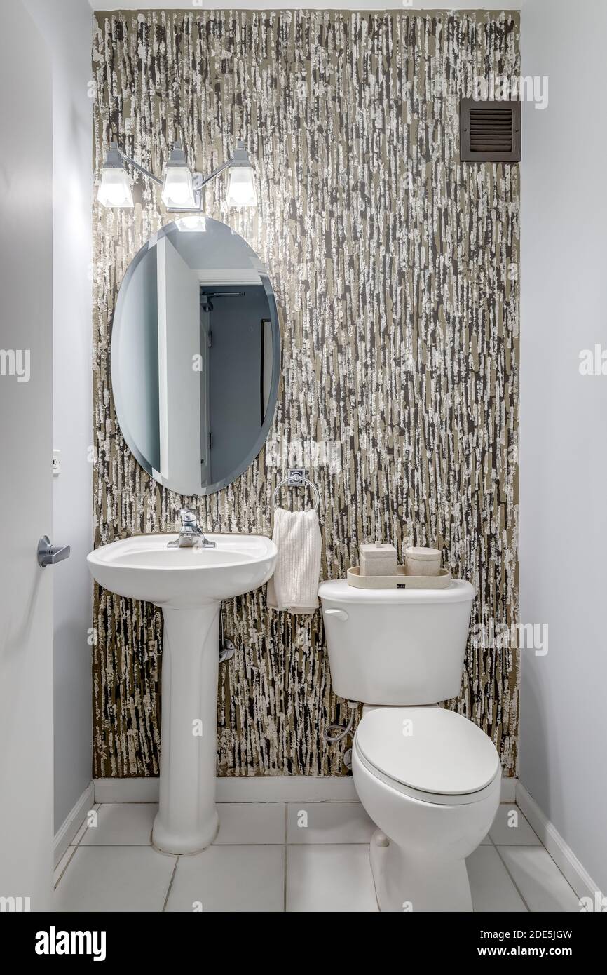 Une petite salle de bains tapissés de papier peint avec un lavabo sur pied blanc au-dessus de carreaux de marbre blanc. Banque D'Images