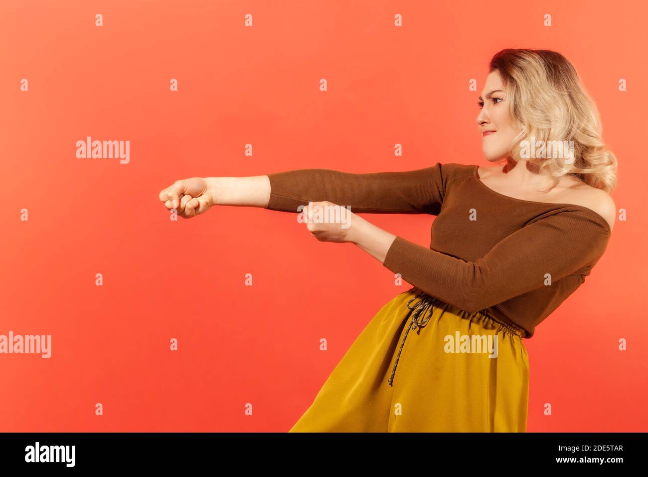 Vue latérale portrait d'une femme ambitieuse forte en blouse brune prétendant tirer la corde invisible, concept de travail dur, effort et les efforts pour réaliser Banque D'Images Vue latérale portrait d'une femme ambitieuse forte en blouse brune prétendant tirer la corde invisible, concept de travail dur, effort et les efforts pour réaliser Banque D'Images