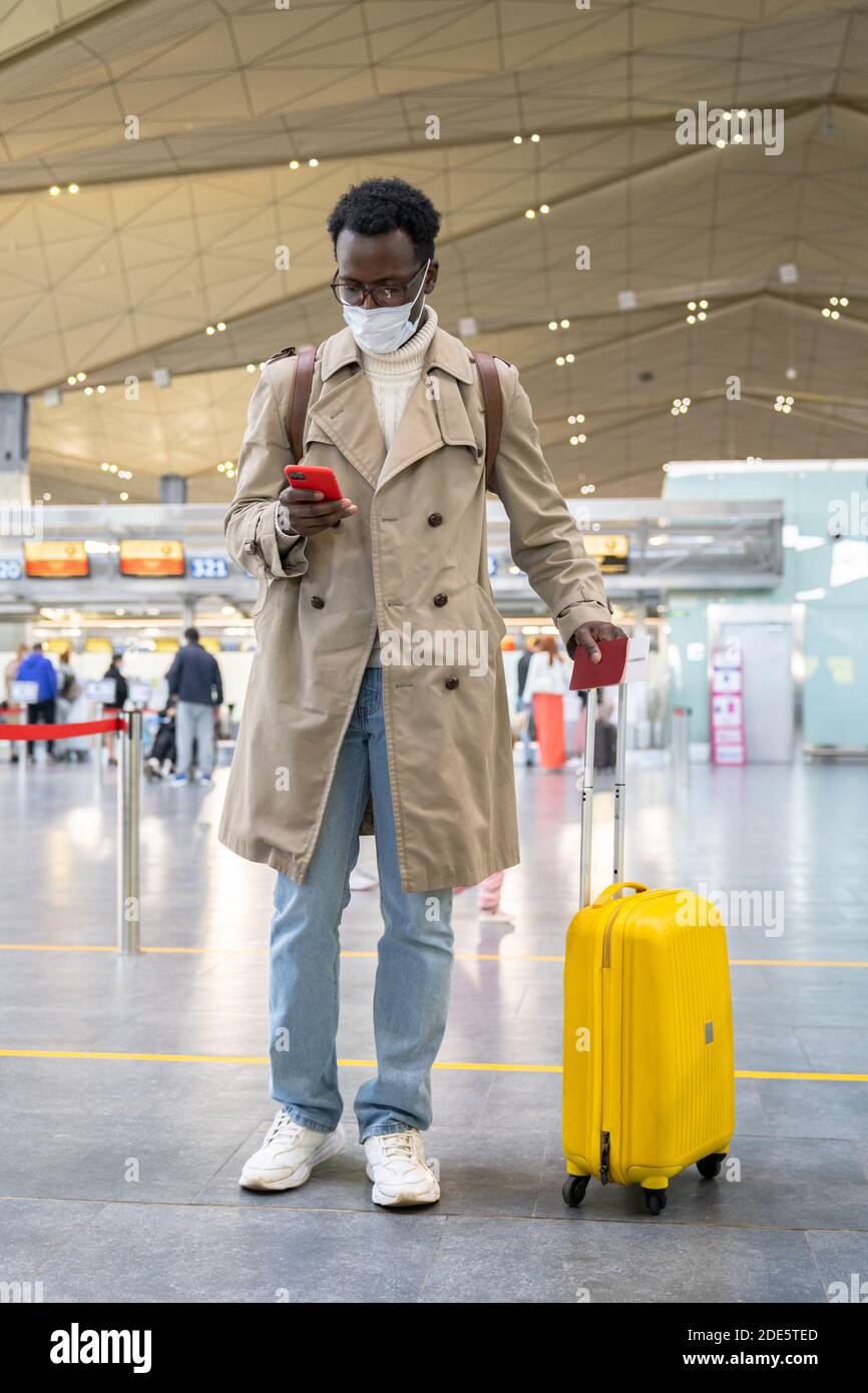 Portrait d'Afro-américain voyageur homme avec valise utilisant le téléphone, portant un masque de protection du visage pendant l'épidémie de virus, coronavirus, covid-19 pandémie W Banque D'Images