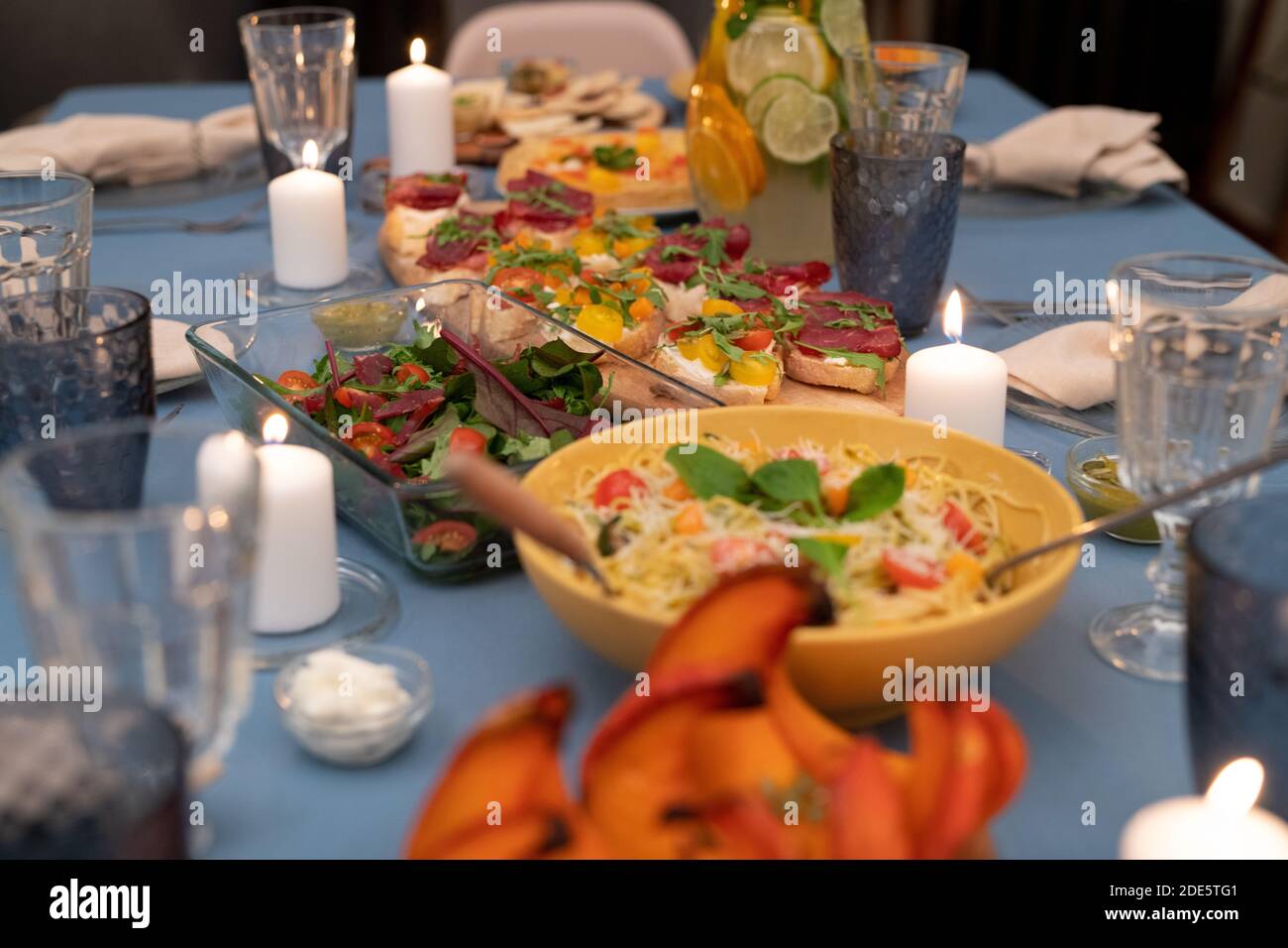 Partie de la table de fête servie avec des verres à vin, bougies allumées, salade de légumes, sandwichs maison avec des tomates fraîches et des pâtes Banque D'Images