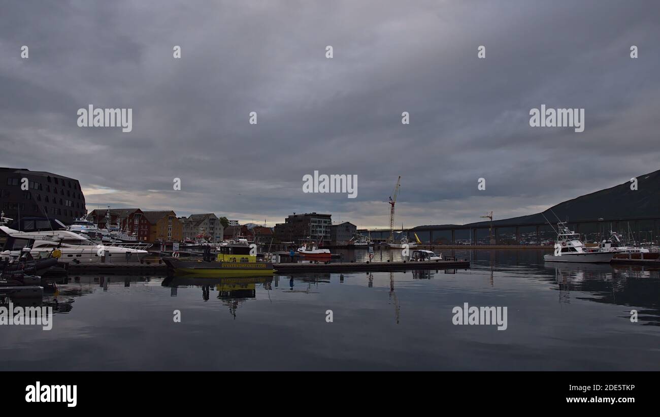 Tromsø, Norvège - 08-23-2020: Port paisible de Tromsø avec des bateaux d'amarrage et le stade d'atterrissage se reflète dans le calme de l'eau et le pont routier de Tromsørua. Banque D'Images