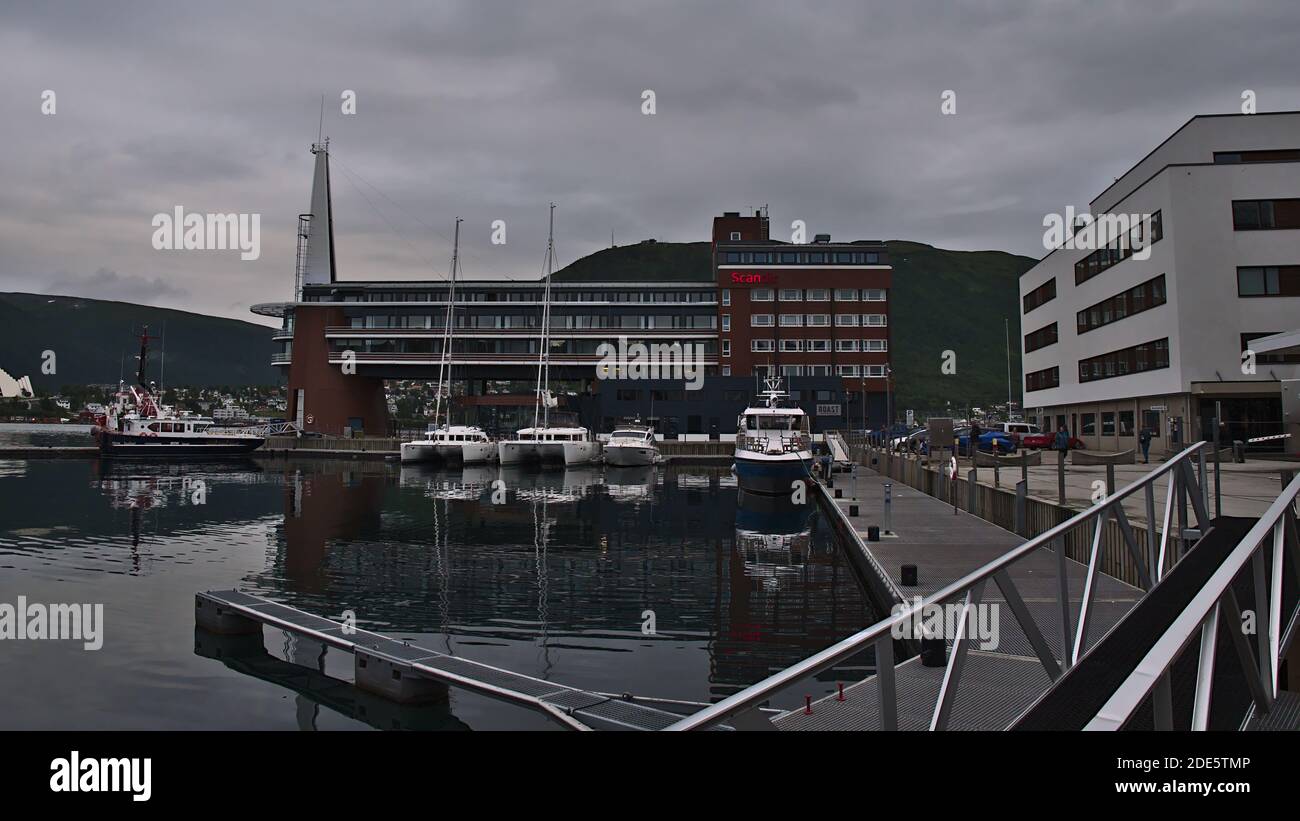 Tromsø, Norvège - 08-23-2020: Port de la ville norvégienne Tromsø avec des bateaux d'amarrage dans l'eau calme et l'hôtel Scandic Ishavshotel (architecture moderne). Banque D'Images