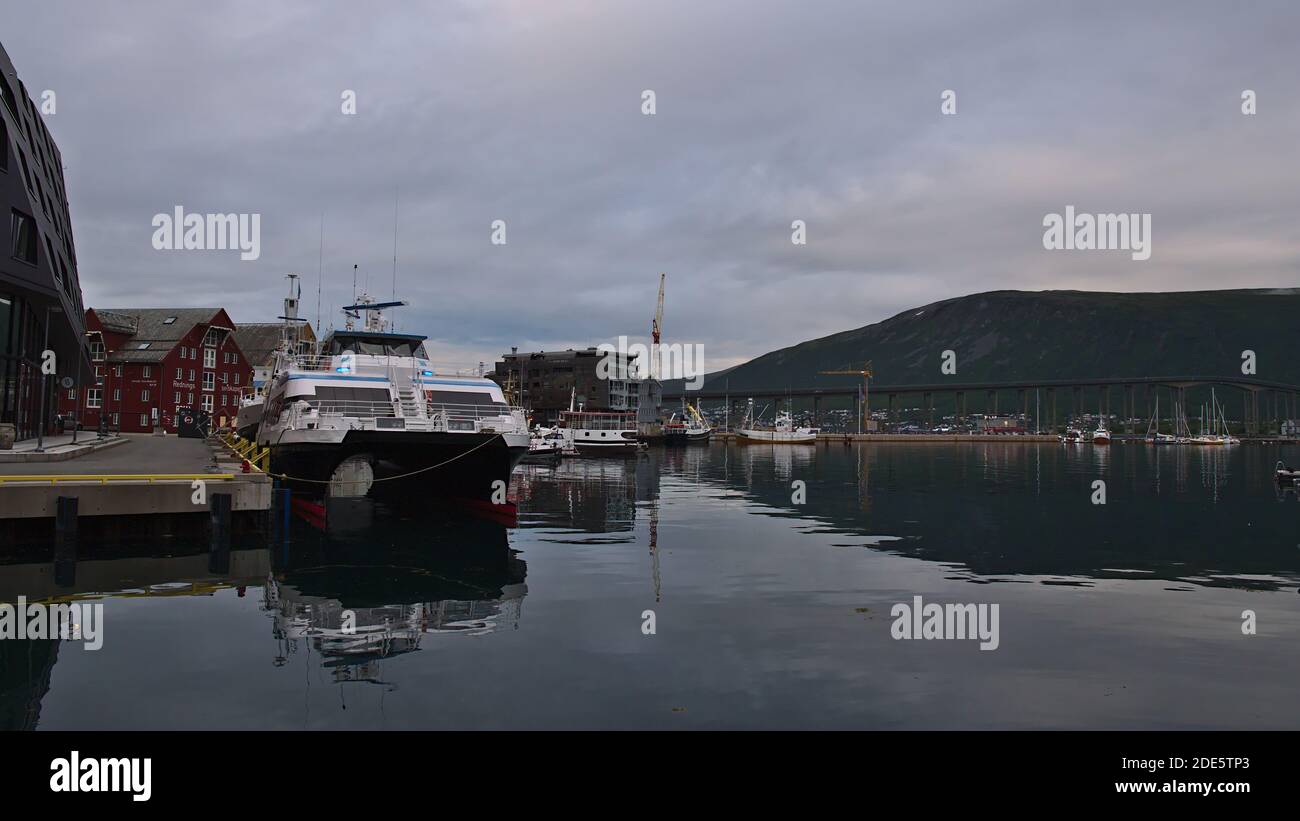 Tromsø, Norvège - 08-23-2020: Port calme de Tromsø avec bateaux d'amarrage et pont routier de Tromsøbrua en arrière-plan lors d'une journée nuageux à la fin de l'été. Banque D'Images