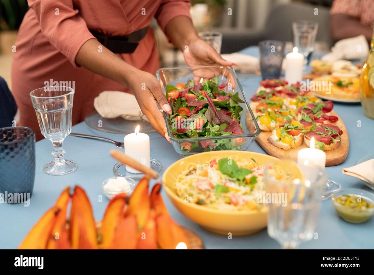 Mains de la jeune femme africaine mettant bol en verre avec frais salade de légumes servie sur une table de fête avec des sandwiches faits maison et pâtes Banque D'Images
