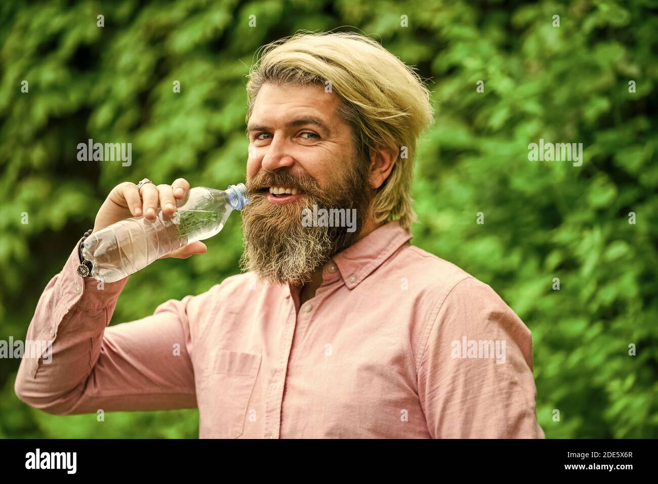 il faut boire un verre. un homme brutal boit de l'eau. un homme barbu tient une bouteille d'eau en plastique. il a soif. buvez un peu d'eau en marchant dans le parc. rafraîchissez-vous. Maintenir l'équilibre de l'eau dans le corps. Banque D'Images