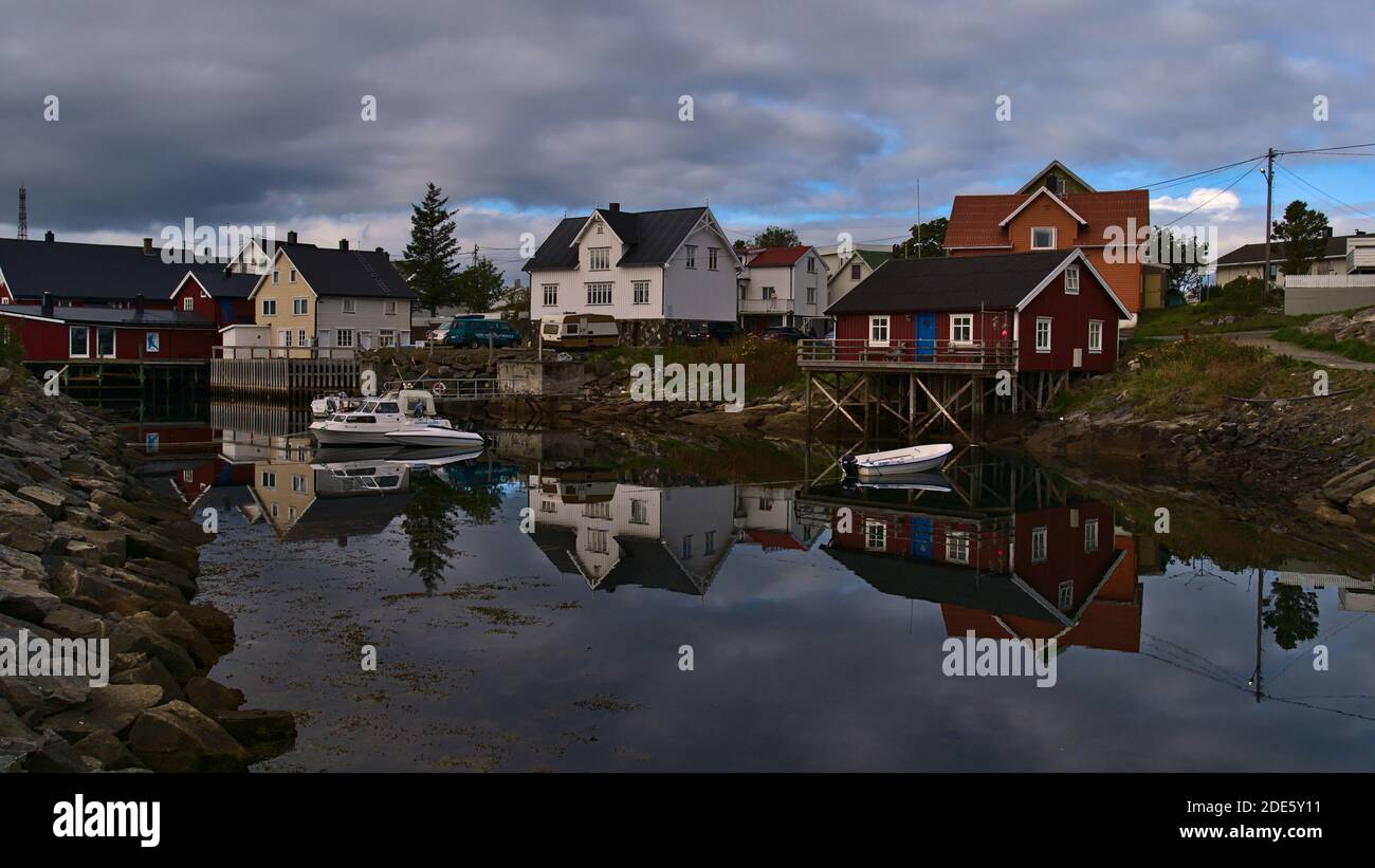 Henningsvær, Austvågøya, Lofoten, Norvège - 08-29-2020: Maisons traditionnelles en bois et corbu rouge (maison de pêcheur sur pilotis) avec bateau d'amarrage. Banque D'Images