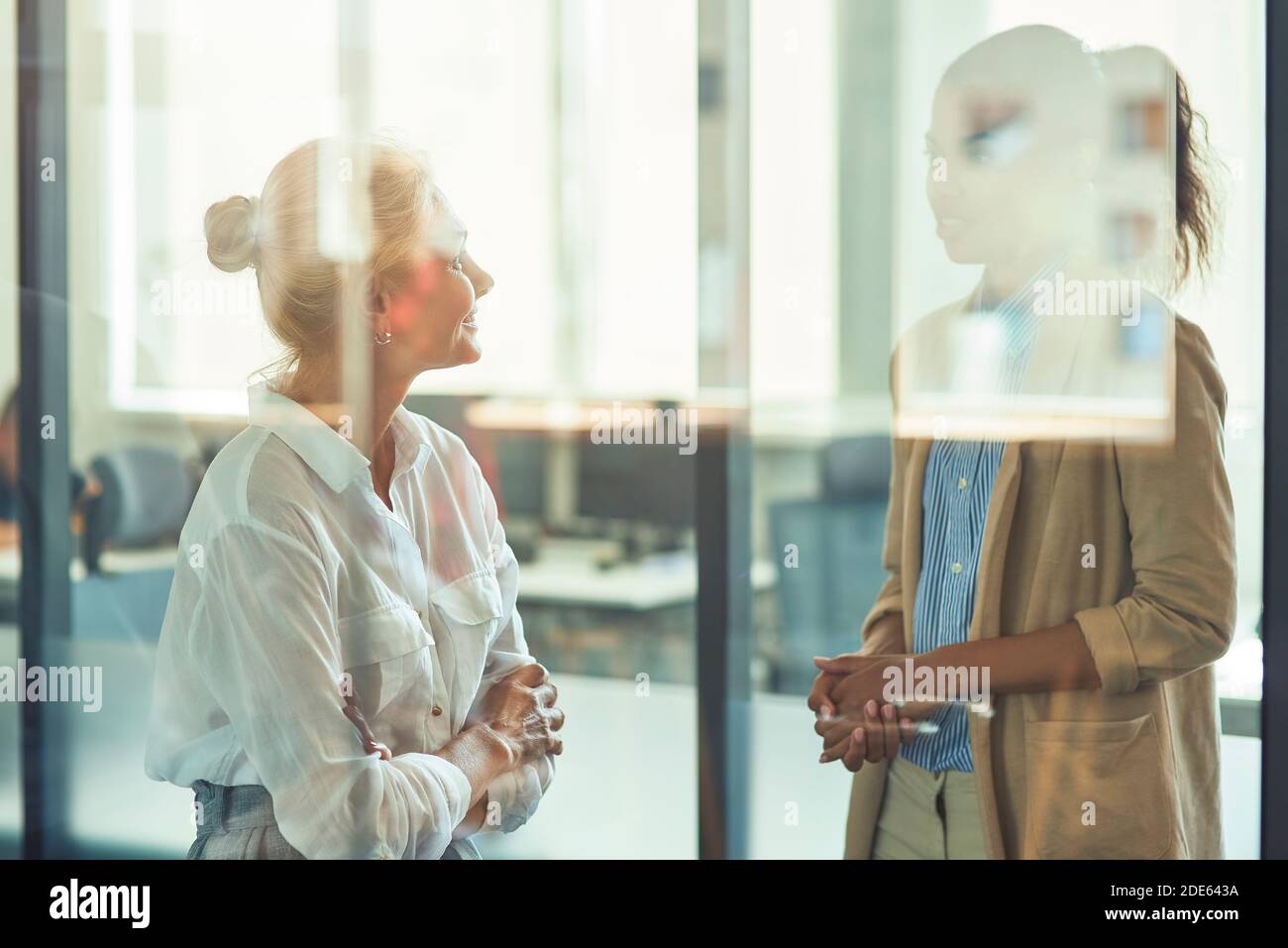 Deux collègues féminins différents ayant une conversation informelle tout en restant debout le bureau moderne Banque D'Images