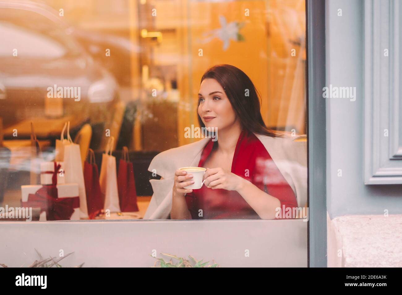 Portrait belle fille heureuse dans élégant manteau boire café et regarder dans la fenêtre dans le café du centre commercial. Jeune belle femme élégante appréciez le cappuccino chaud en res Banque D'Images