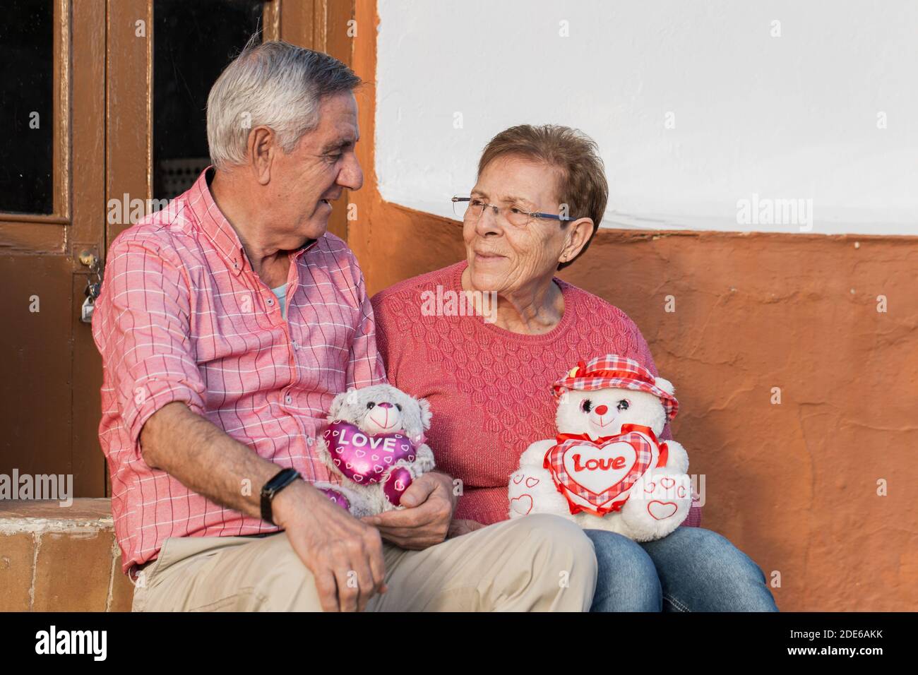 Positif homme âgé et femme en tenue décontractée tenant mignon jouets avec cœur et regardant l'un l'autre avec amour Tout en célébrant la Saint Valentin Banque D'Images
