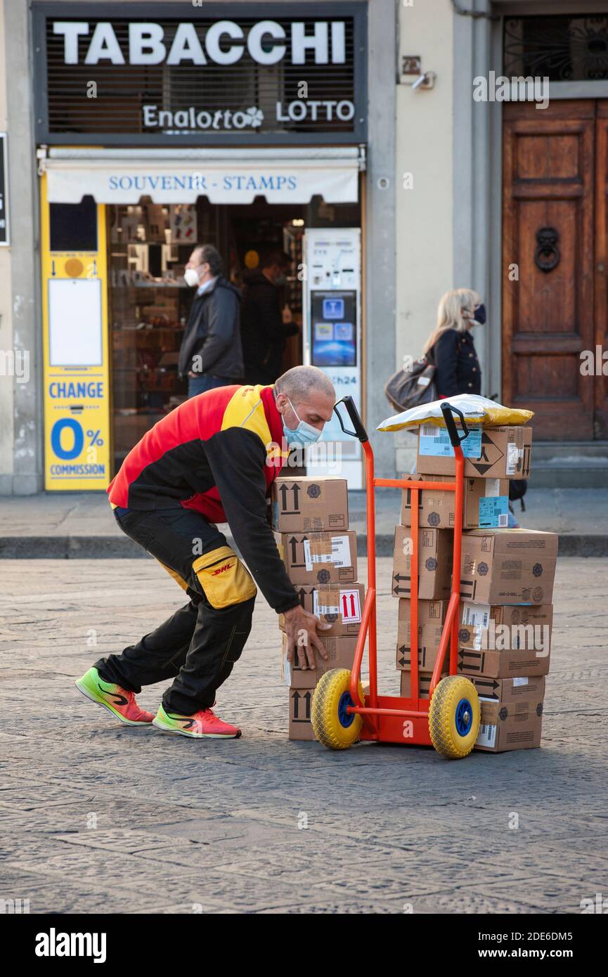 Florence, Italie - 2020, 19 novembre : un liveur DHL dans une rue, prêt pour la livraison du colis, portant un masque de protection, pendant la pandémie Covid-19 Banque D'Images