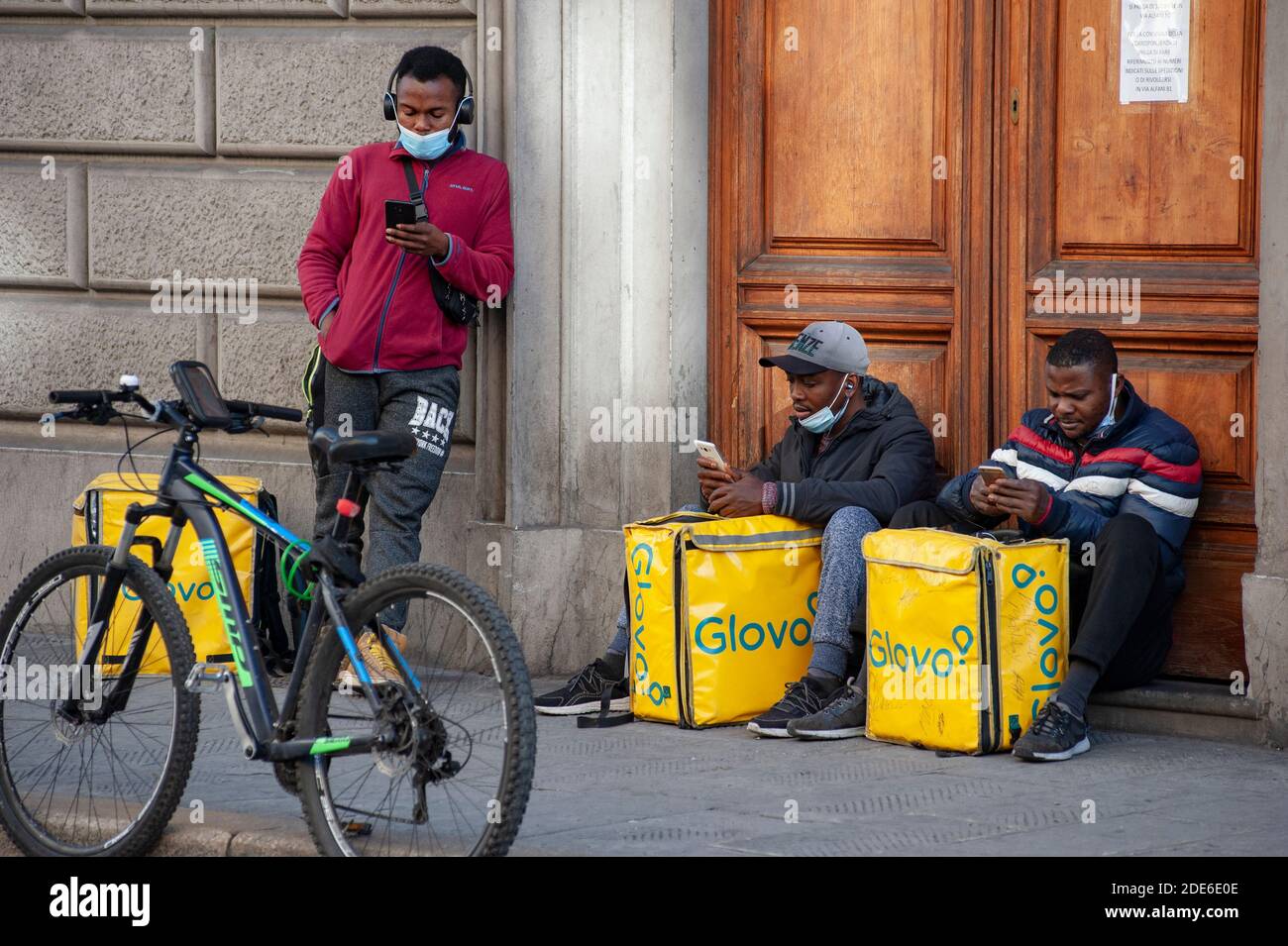 Florence, Italie - 2020, 19 novembre : des cavaliers debout dans la rue, prêts à livrer de la nourriture en ville, pendant le confinement de Covid-19. Africain jeune homme. Banque D'Images